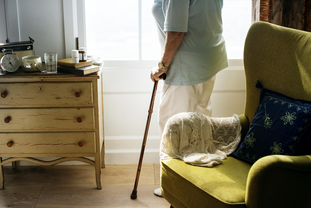 A person holding a cane standing in a living room inside a house.