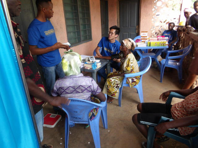 Kevin Liu (blue shirt, sitting in chair), a VCU medical student, works with patients and colleagues in the village of Achem in Ghana's Volta region.