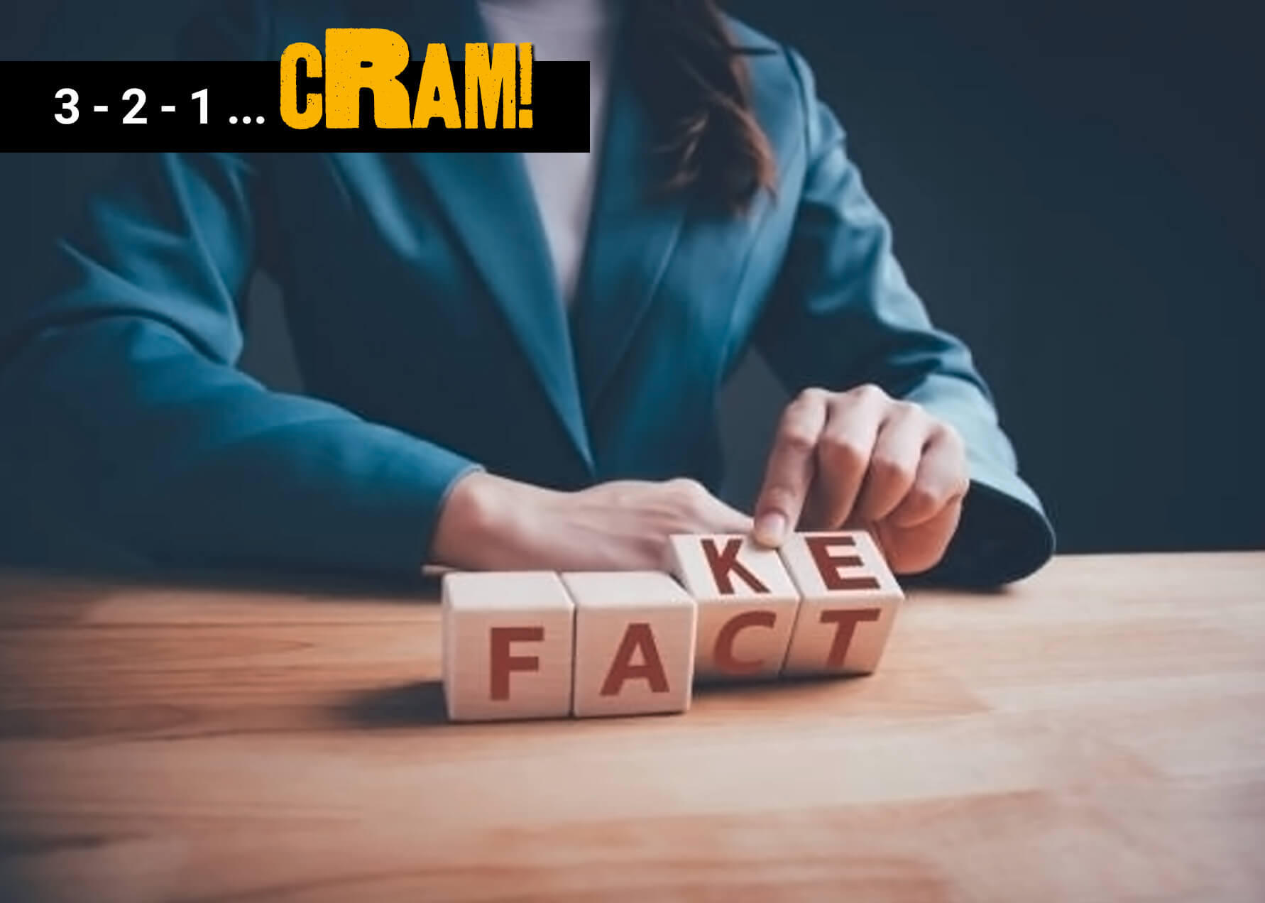 A photo of the torso of a person sitting at a table. They are moving some wooden blocks with letters on them. The first to blocks say \"FA\" and the second two say \"KE\" and \"CT\" on either side of them. A black rectangle in the corner says \"3-2-1 ...\" in white text and \"cRAM!\" in yellow text.