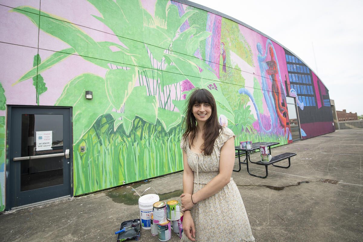 A photo of a woman standing in front o a mural. 