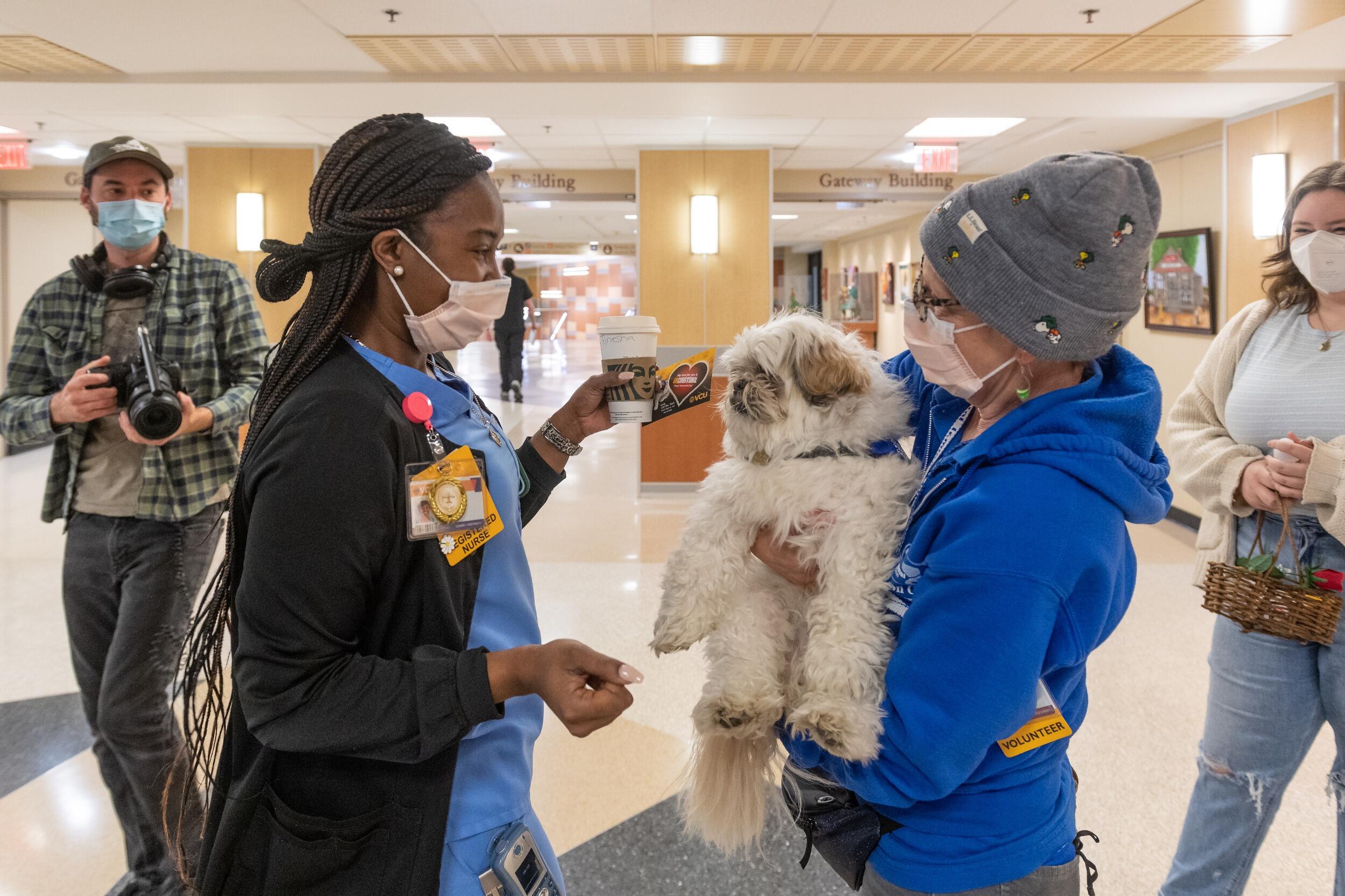 Woman in scrubs holding a valentines card and interacting with a therapy dog.