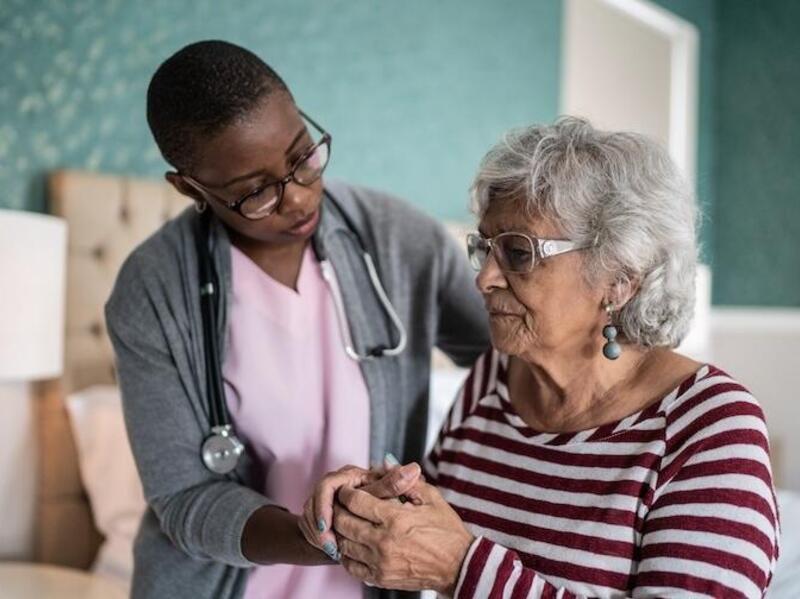 A photo of a woman wearing a stethoscope holding the hand of an older woman. 