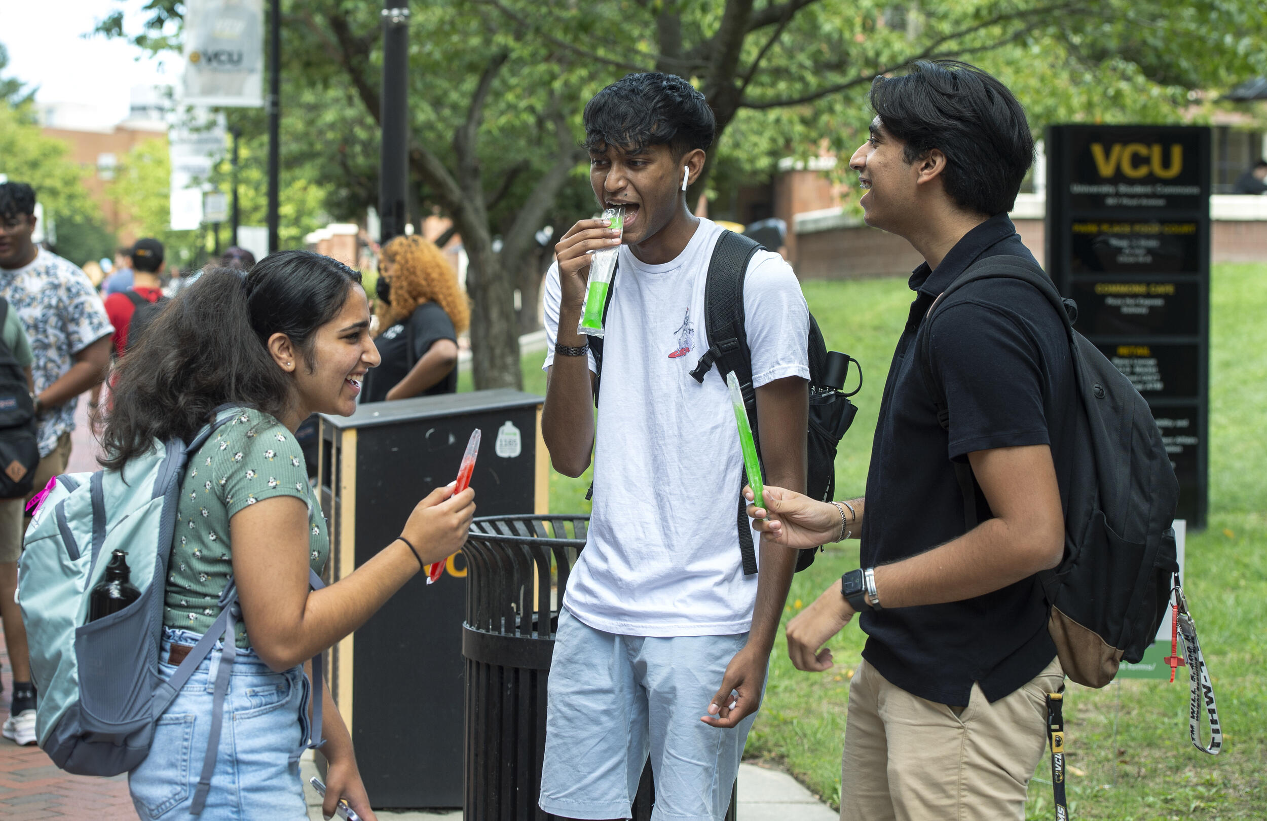 Three students standing in a circle talking to each other while eating ice pops 