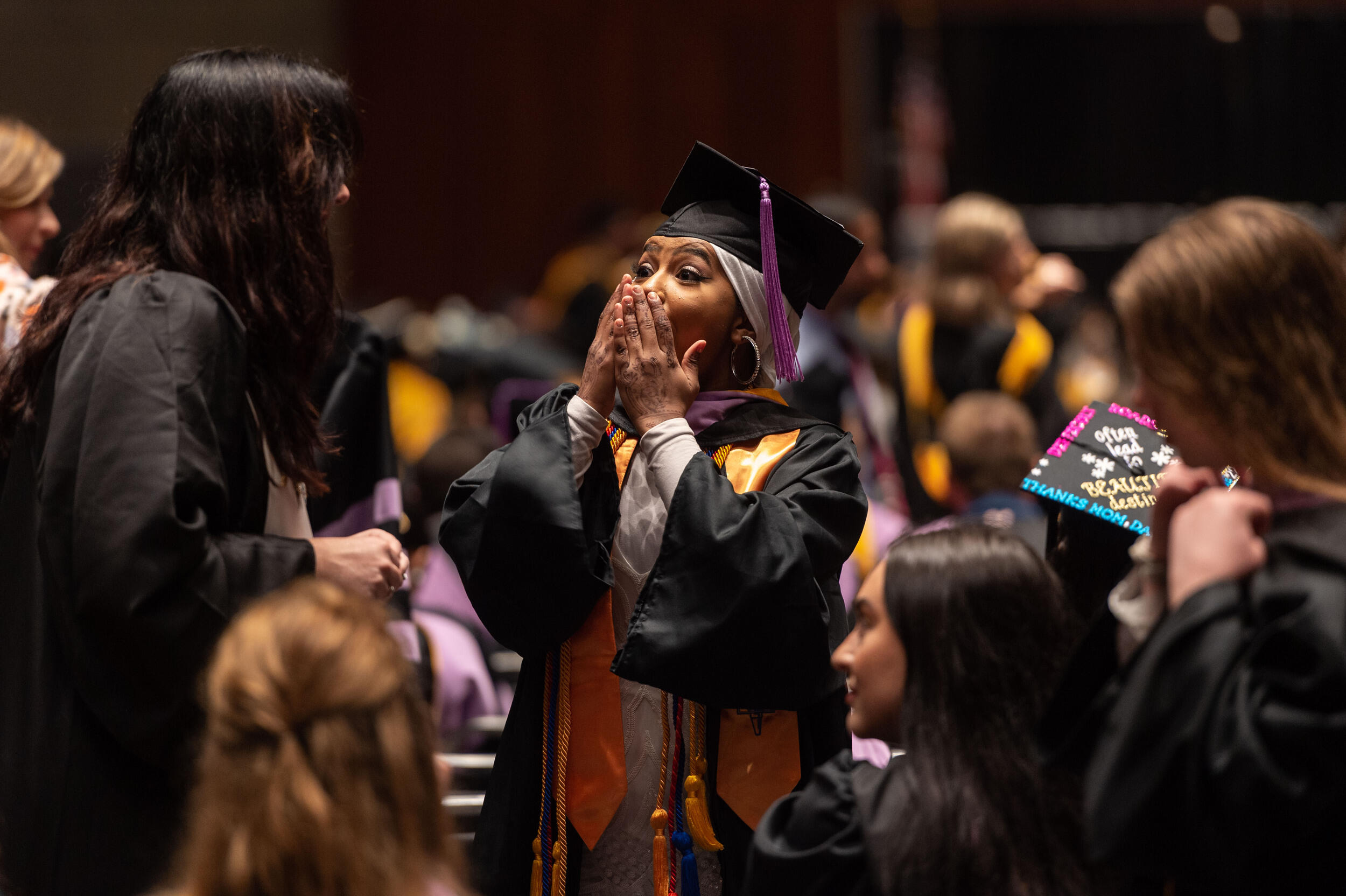 A student in cap and gown holds her hands to her face in excitement. 
