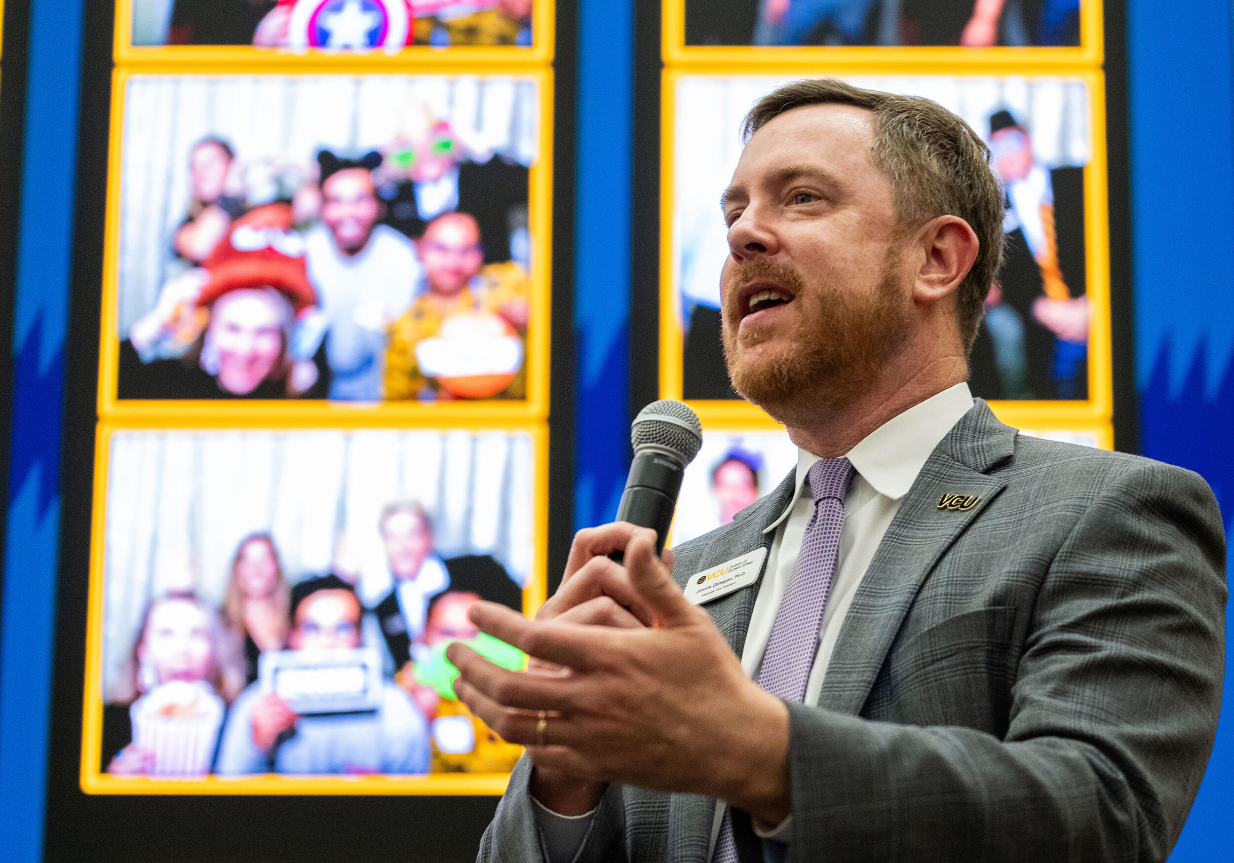 A photo of a a man on a stage holding a microphone and speaking. 