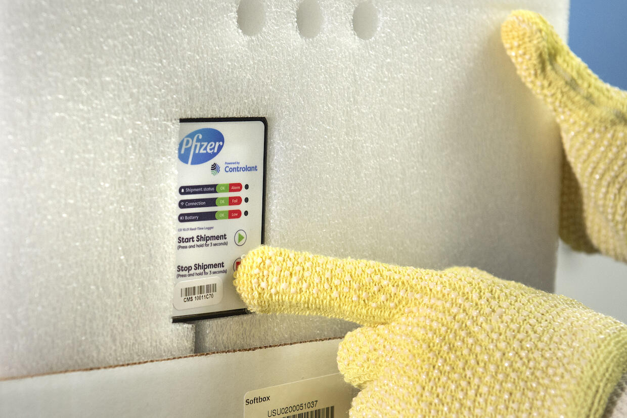 a gloved hand pointing to a temperature control unit on a package of ultra-cold stored COVID-19 vaccine