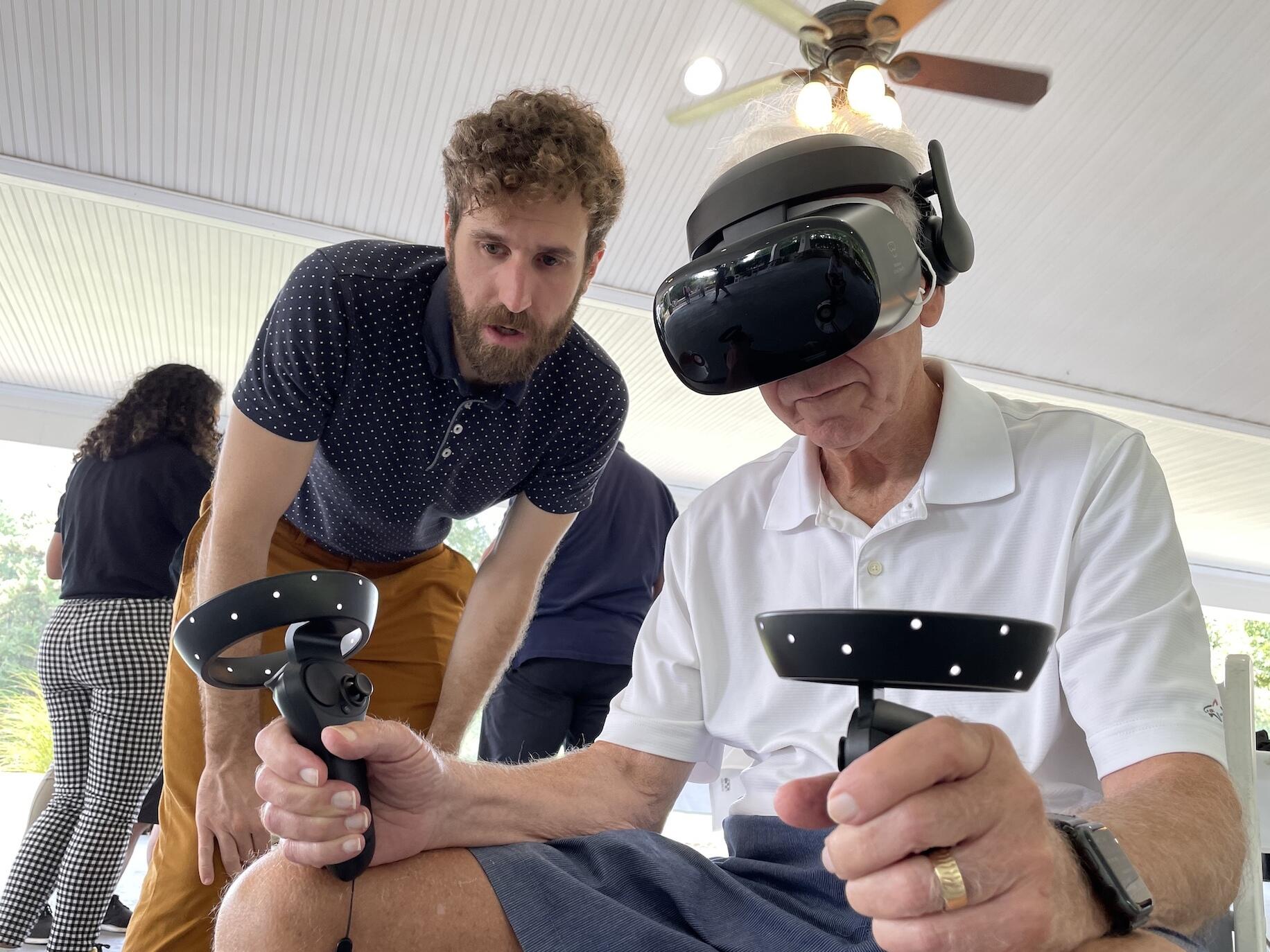 Alexander Stamenkovic, a post-doctoral fellow in the Motor Control Lab, assists Ray Birk as Birk uses a VR headset and hand controls.