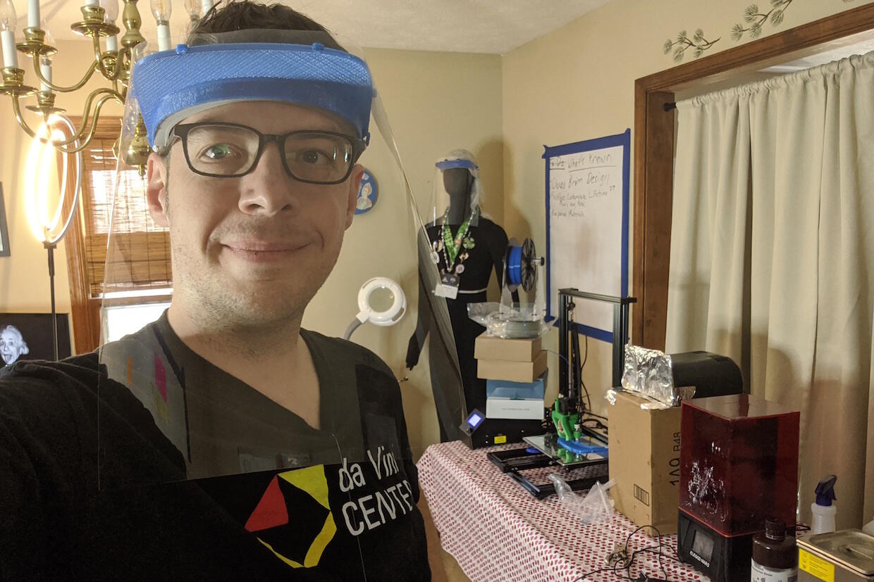 A student wearing a face shield stands in a room with equipment and various items.
