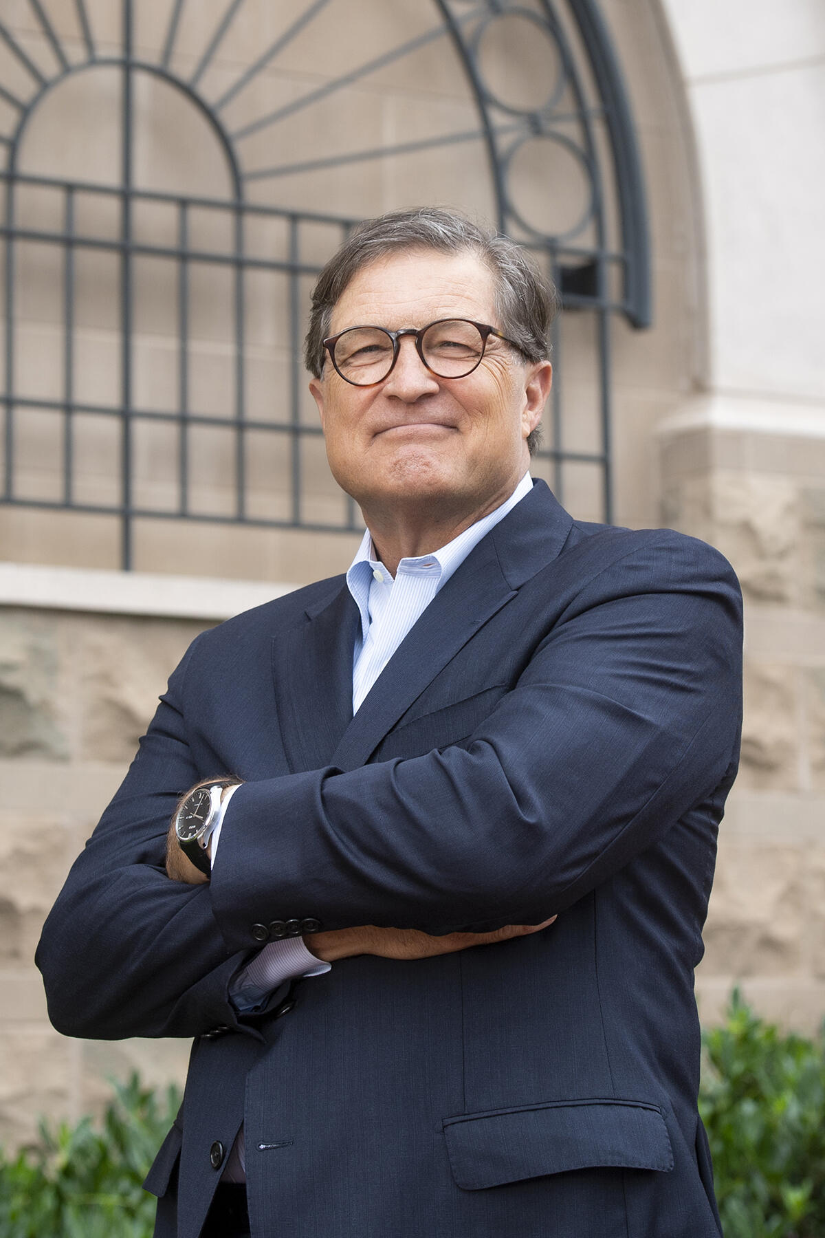 Jeffrey Lacker wearing a navy suit, glasses and a light blue and white shirt. He is staring at the camera with his arms crossed