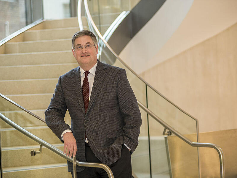 Man in suit standing in front of staircase.