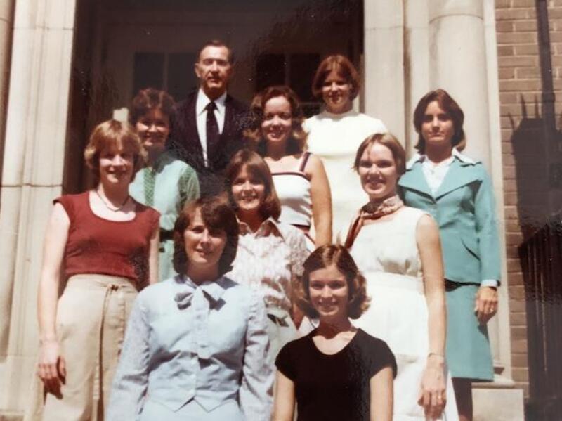 A group photo of nine women and one man standing on the stairs in front of a building. 