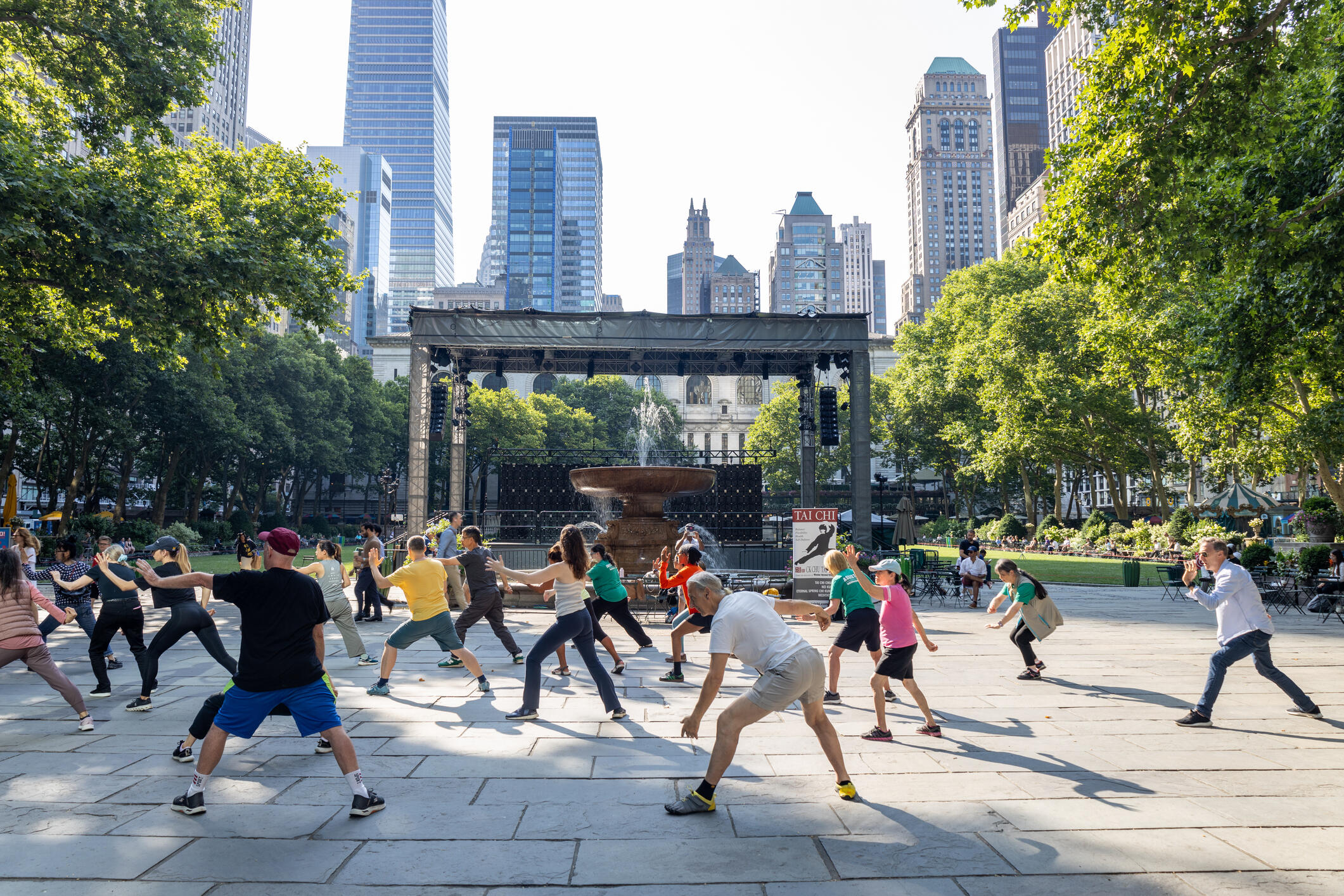 A photo of a large group of people doing a group exercise in a city's public park. 