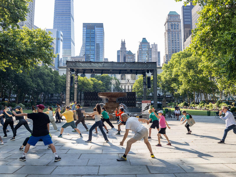 A photo of a large group of people doing a group exercise in a city's public park. 