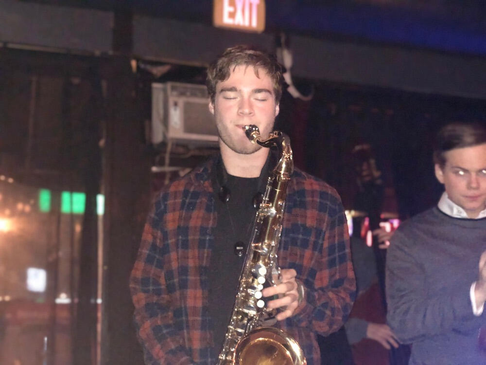 Levine, in red and blue checkered shirt, plays the saxophone. 