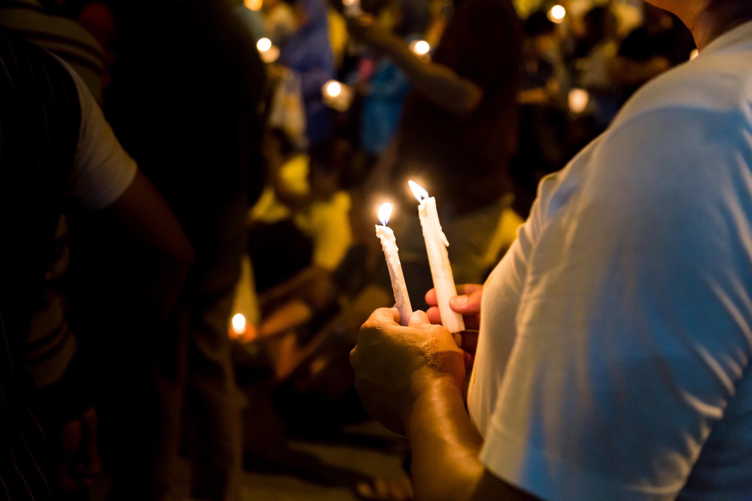 A photo of a person holding two candles in their hands in a crowd of people holding candles. 