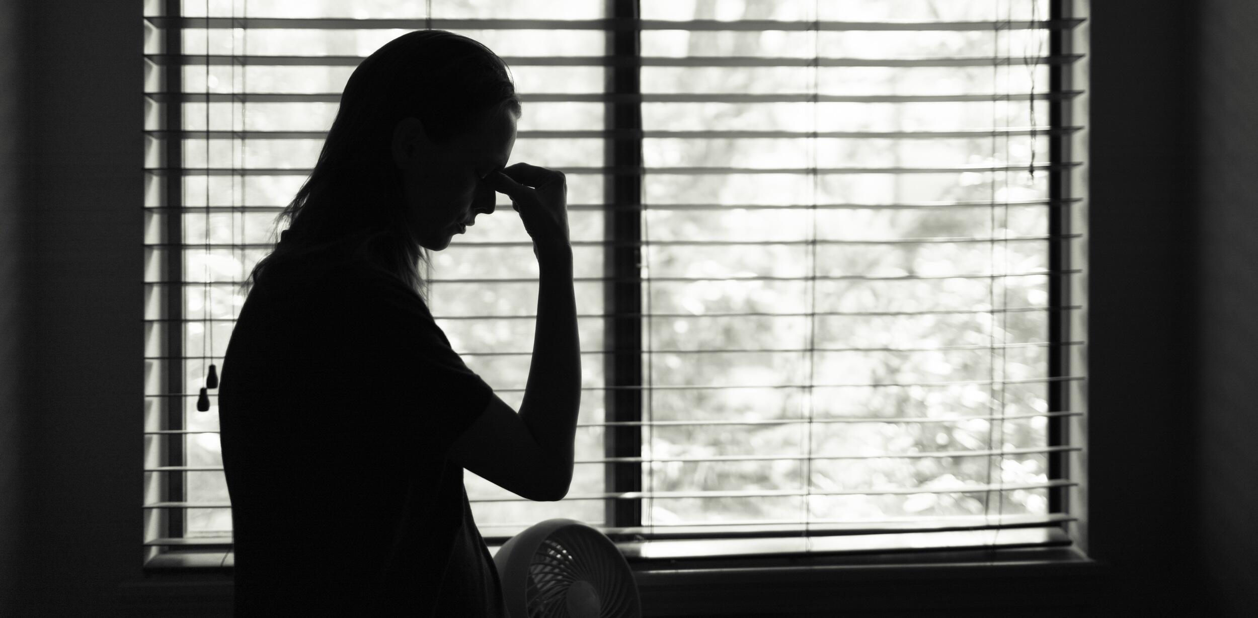 The silhouette woman pinching the brow of her nose in front of a window