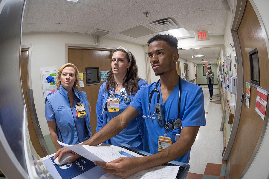 A photo of three people in medical srubs looking at a screen in the hallway of a hospital. 