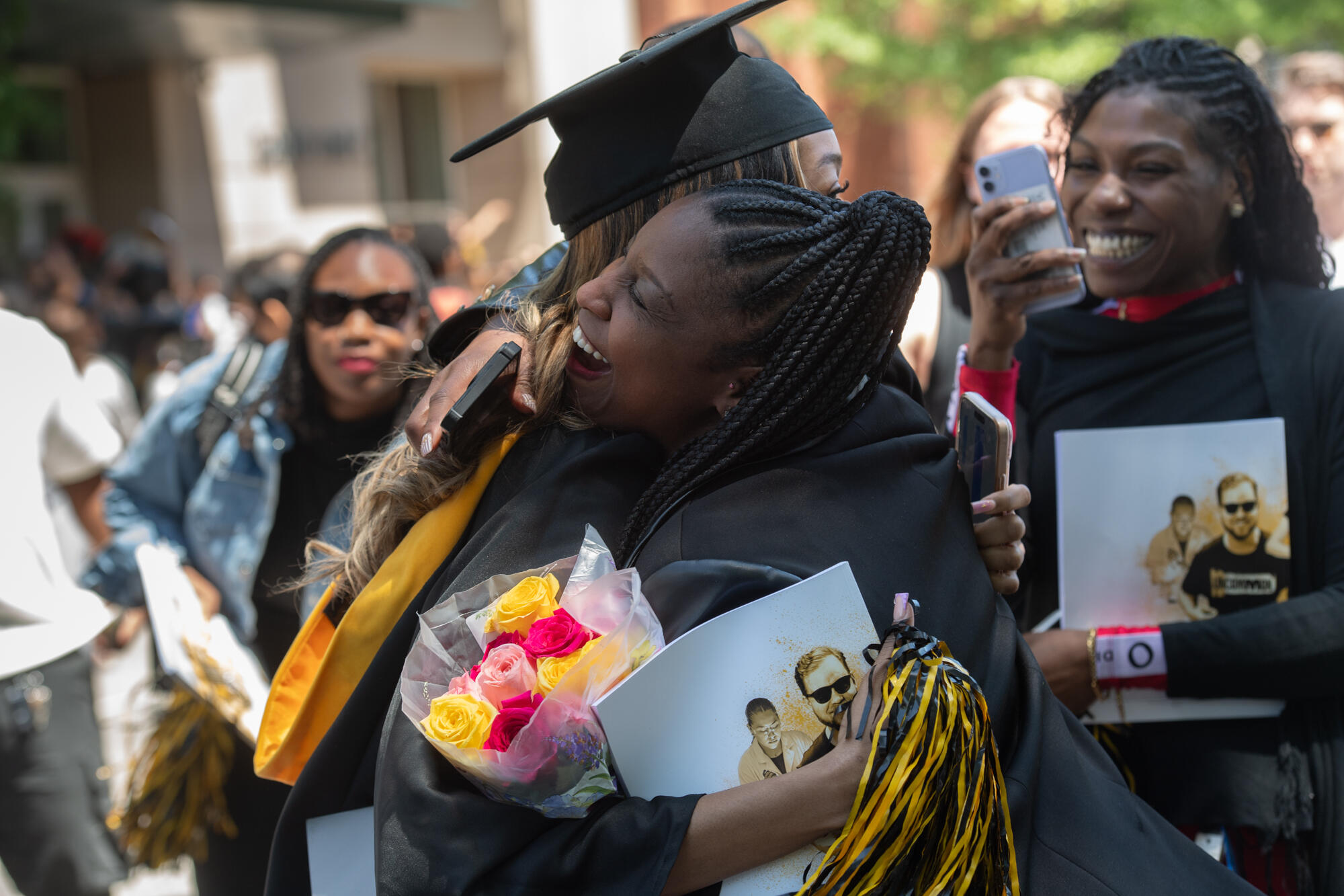 A VCU graduate in cap and gown hugs a woman outside after commencement.