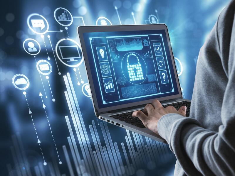 A stock image showing a person typing on a laptop computer displaying a mock security suite. Icons from the suite are displayed in the background the computer.