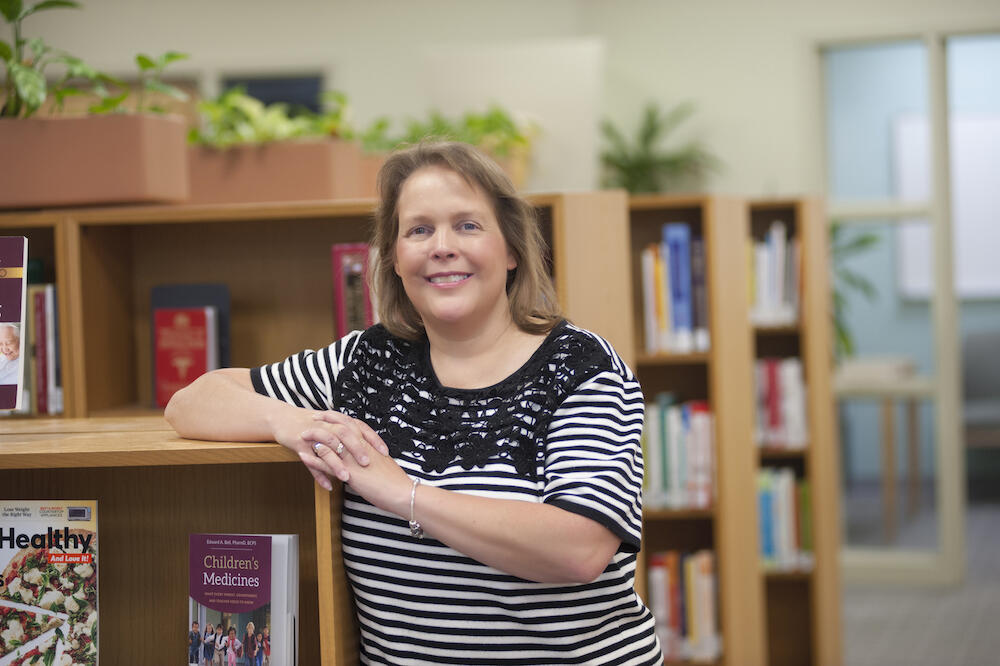 Woman leans and smiles on library bookshelf. 