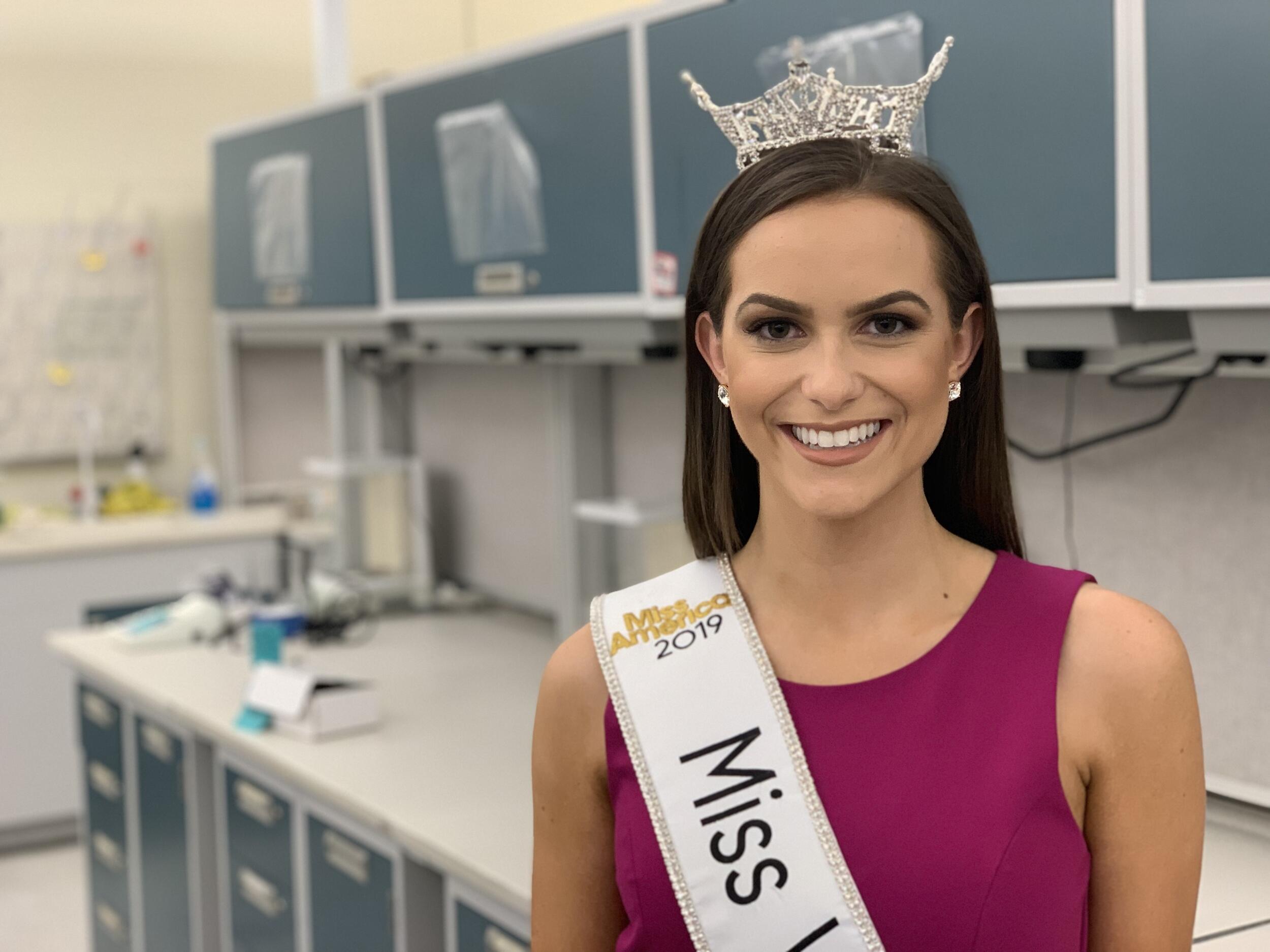 Camille Schrier poses for a portrait inside of a laboratory. She is wearing a Miss Virginia sash and a crown.