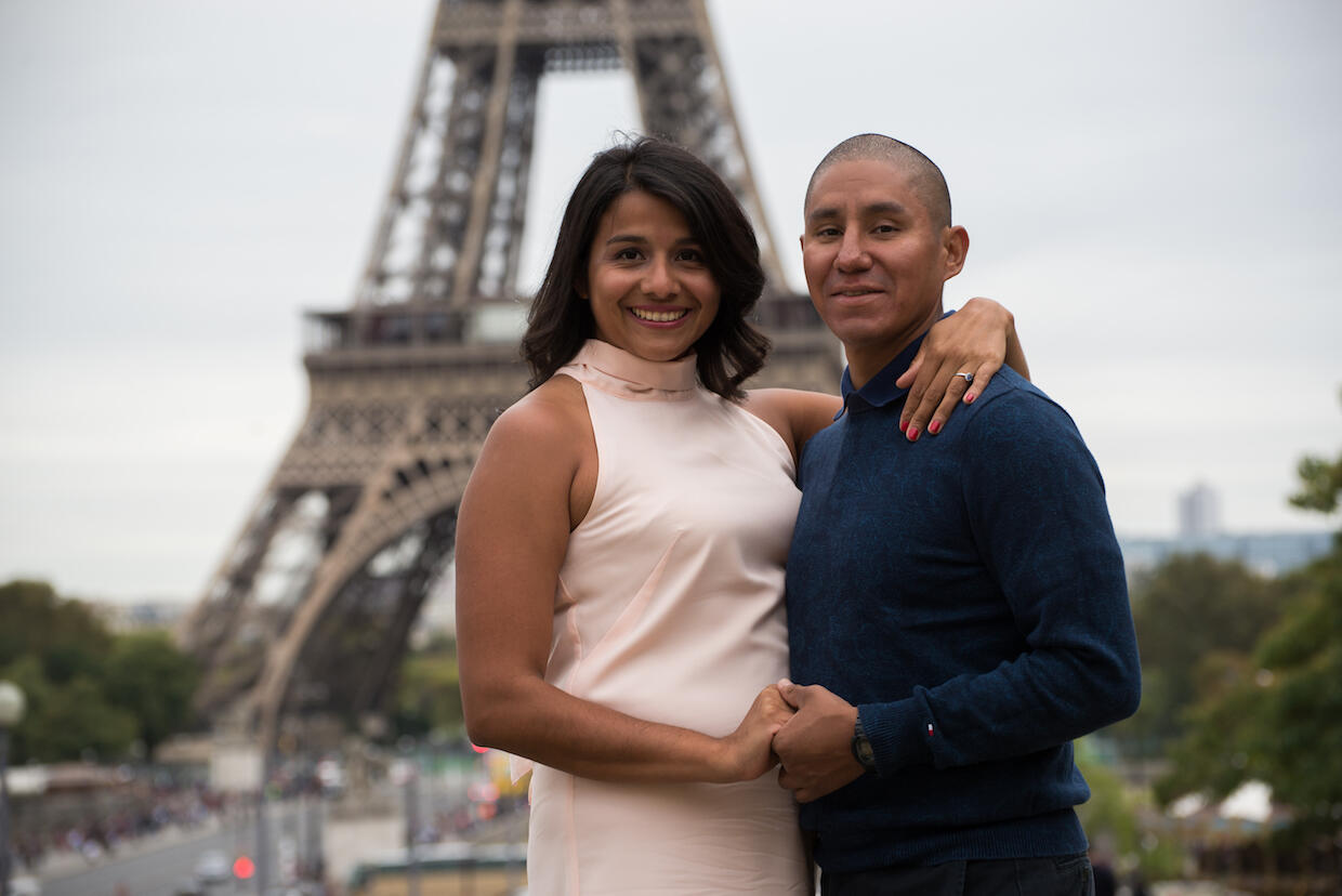 Two people embrace in front of the Eiffel Tower.