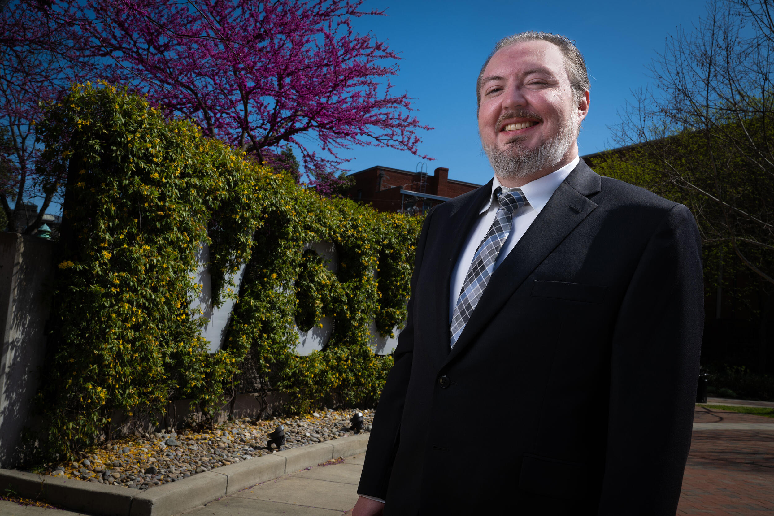 A photo of a man from the waist up. He is standing outside.