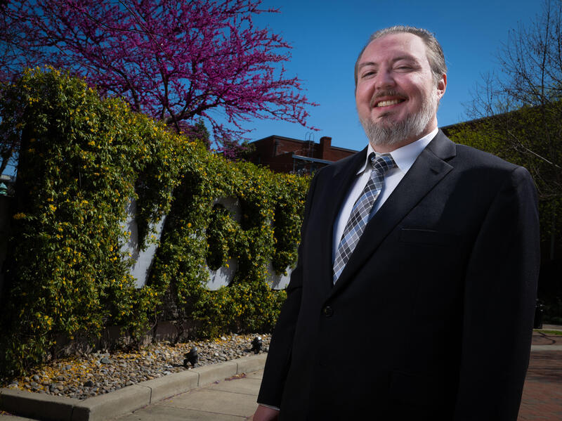 A photo of a man from the waist up. He is standing outside.