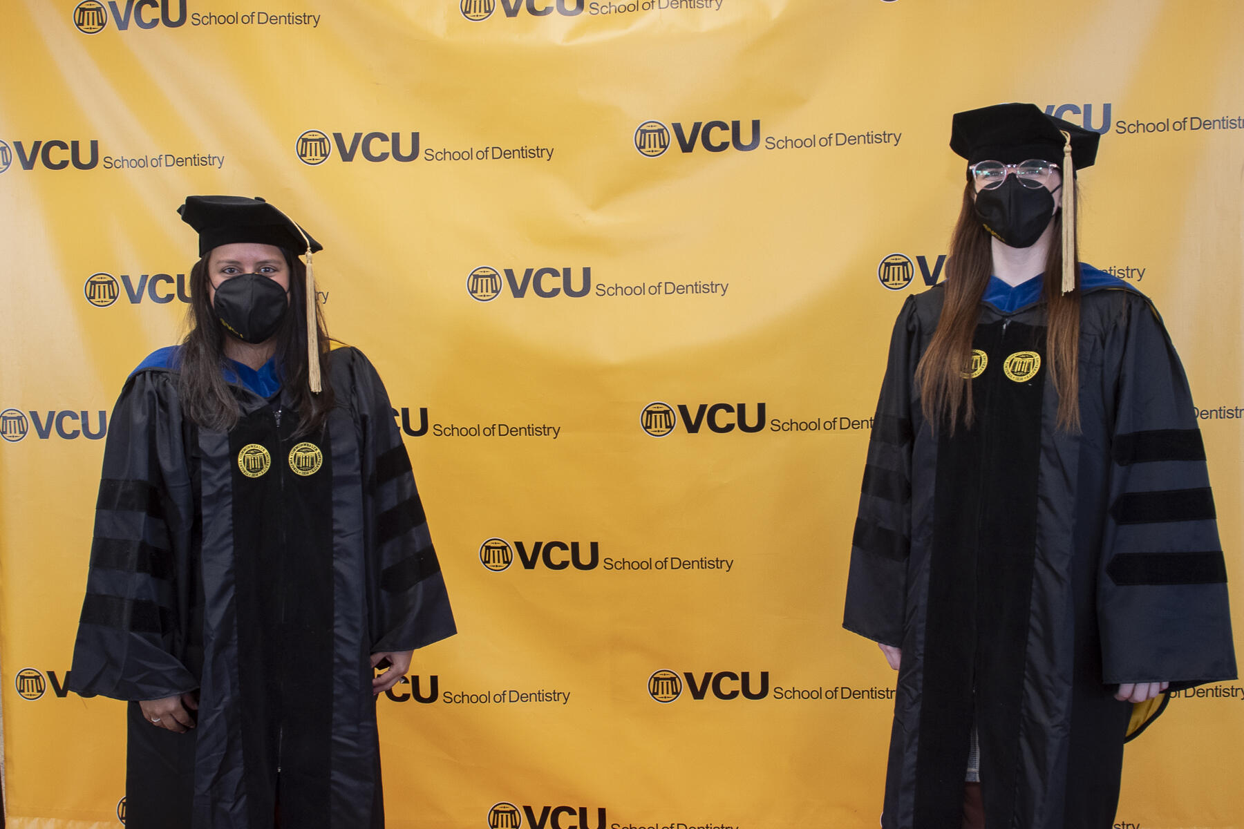 Two students in cap and gown wearing masks.