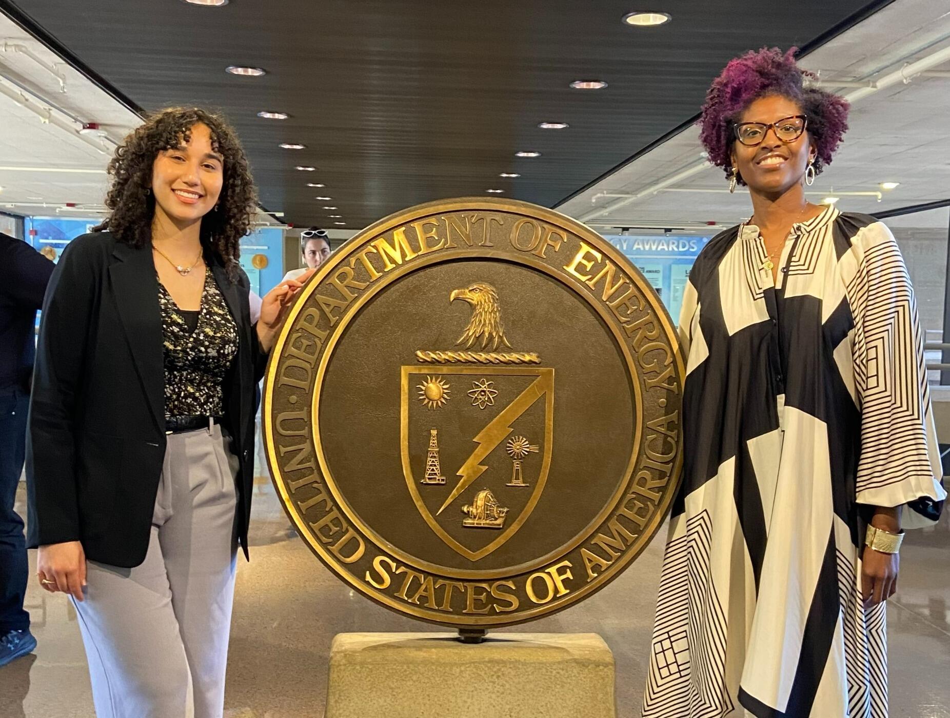 A photo of two women standing on either side of a large metal circle. 