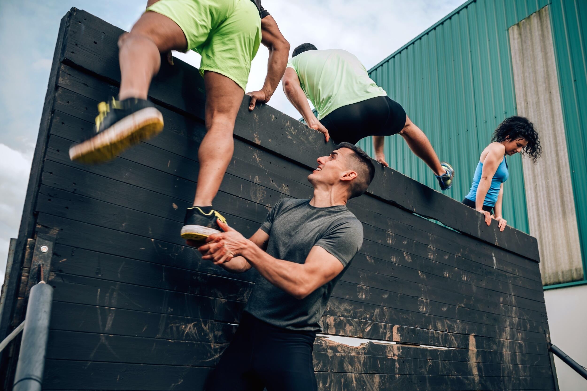People climbing over an obstacle course wall. 
