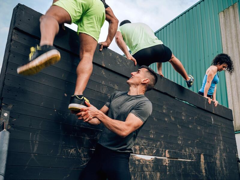 People climbing over an obstacle course wall. 