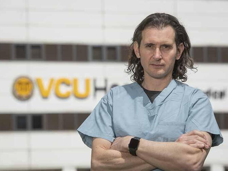 A doctor wearing scrubs with his arms crossed across his chest. 
