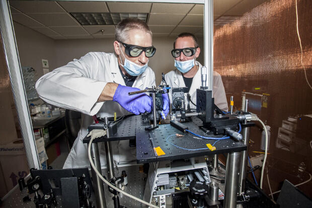Two people in white lab coats work on a machine.