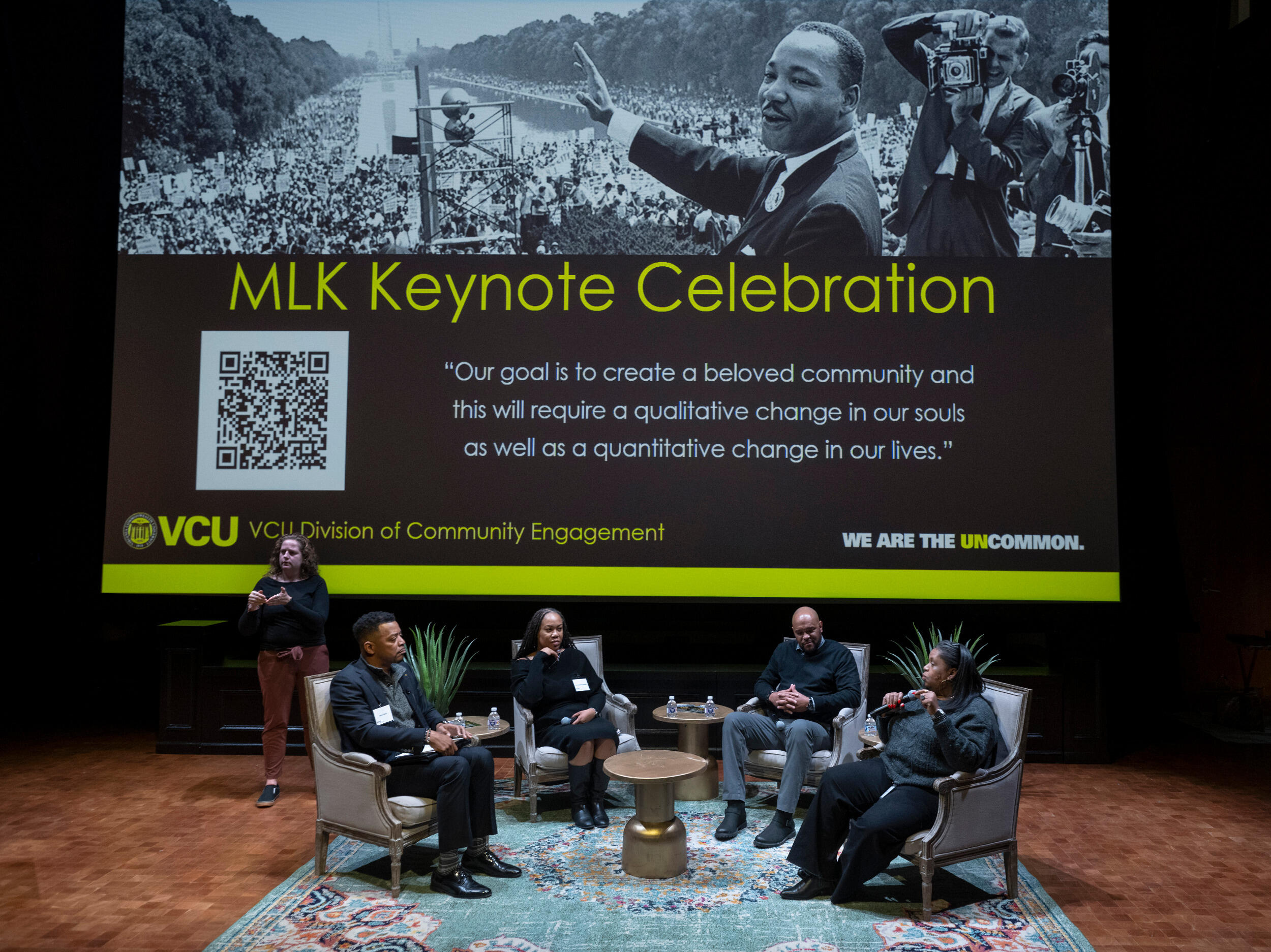 Speakers sit on stage in a semi-circle with an image of Martin Luther King Jr. on the projection screen behind them.