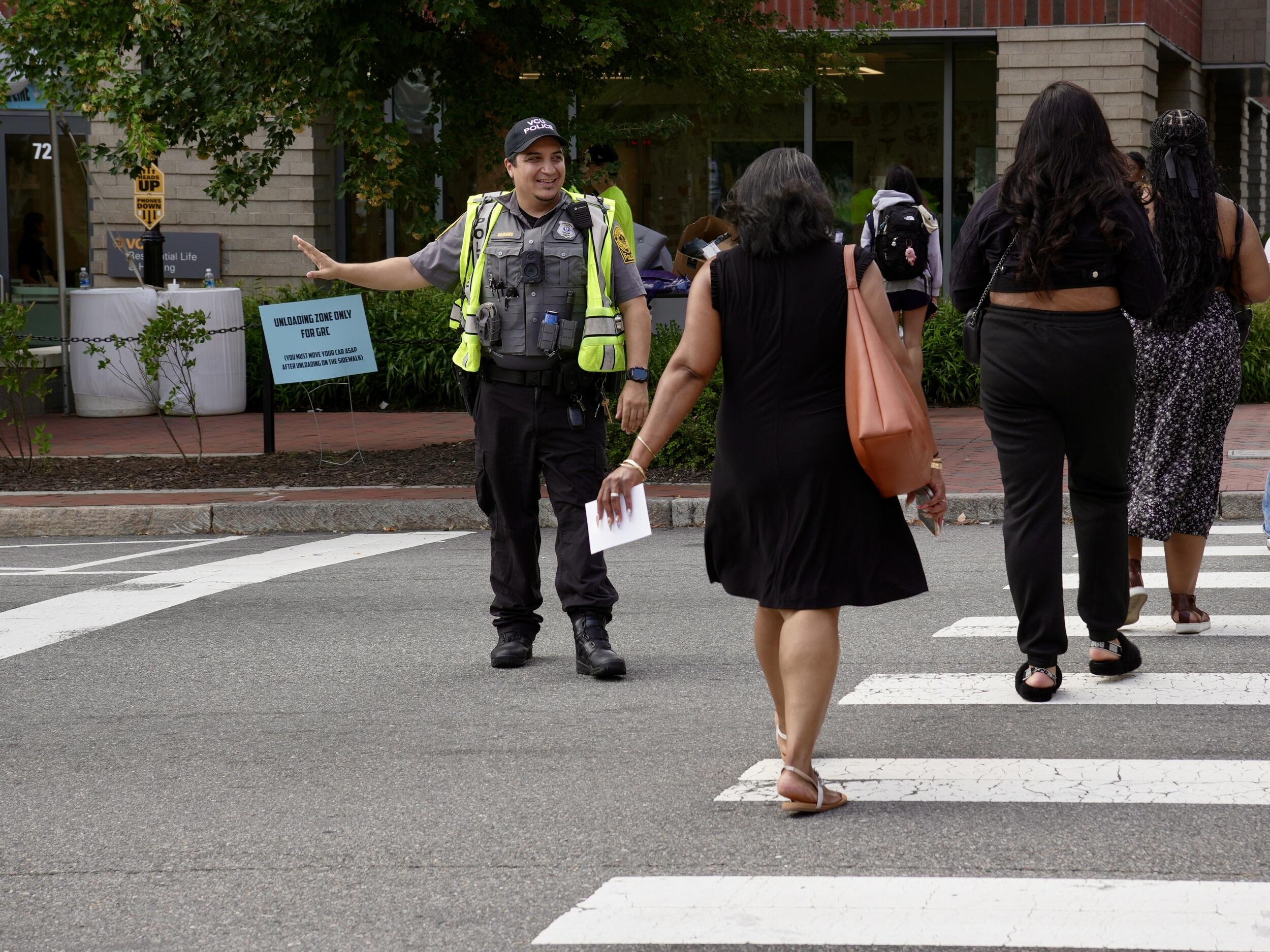 A photo of a police office wearing a yellow visability vest guiding people across a crosswalk. 