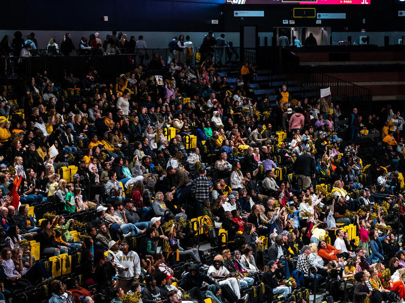 A photo of a crowd of people sitting in the stands at a basketball game. 