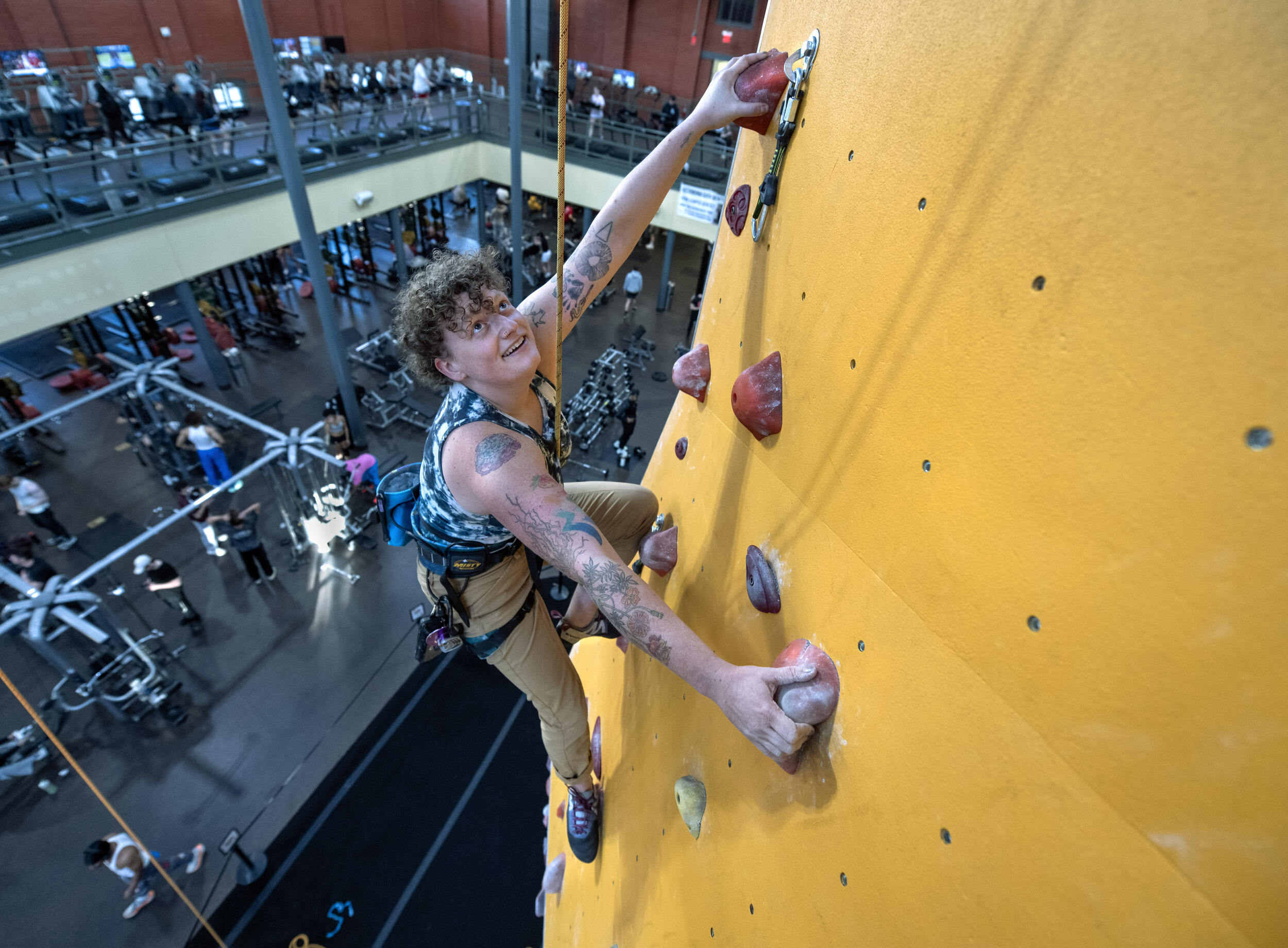 A photo of a person climbing up a yellow rock climbing wall. 