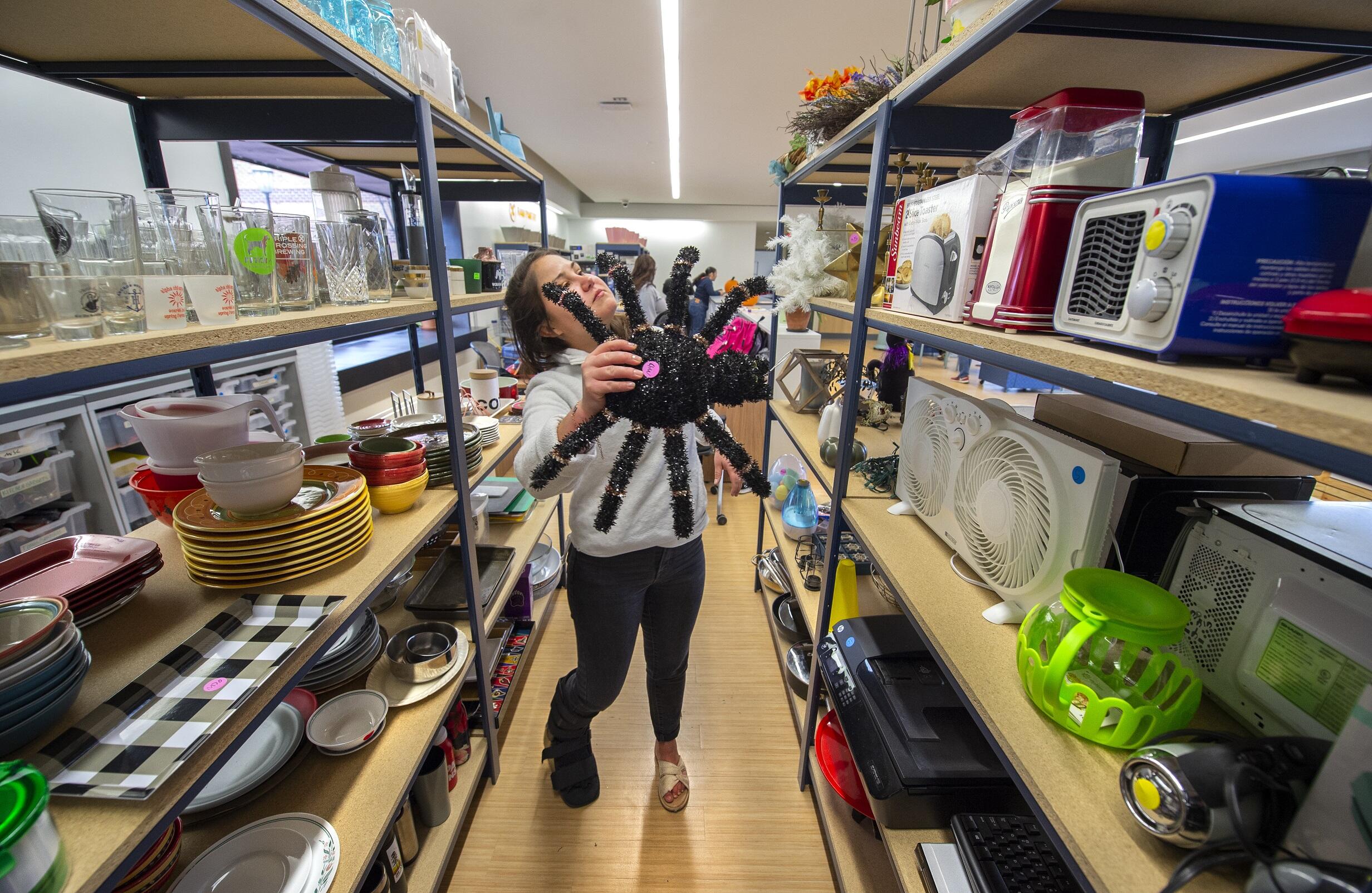 A photot of a woman in an isle between two shelving uinits holding a large fake spider. 