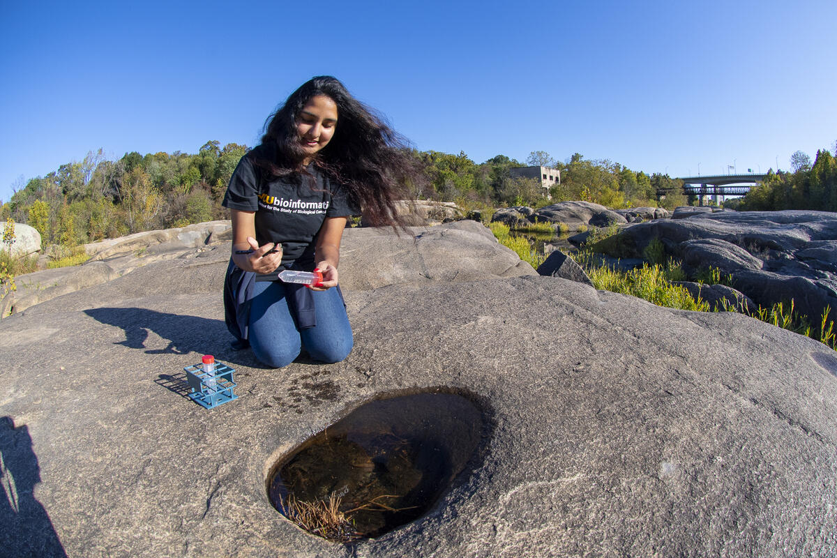 A student holding a water sample kit in front of a rock pool along the James River in Richmond, Virginia.