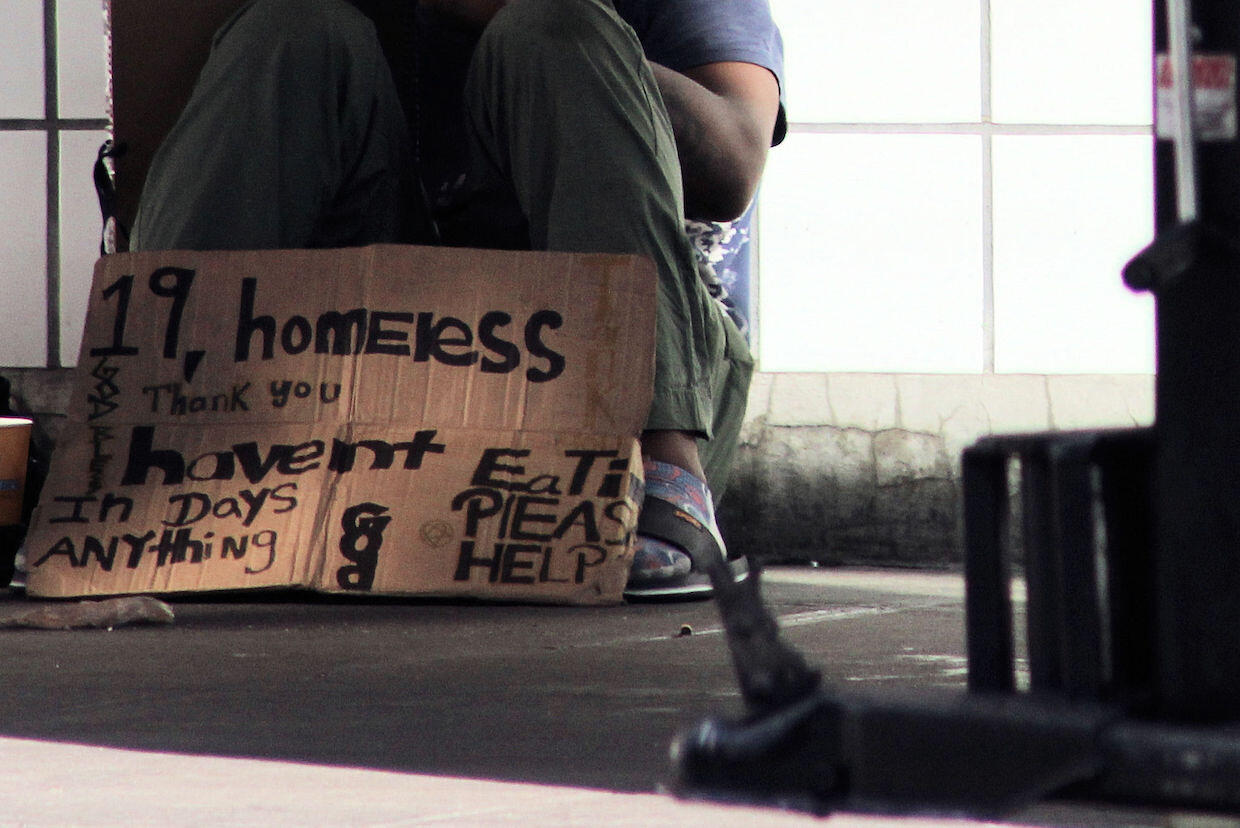 Homeless teenager sitting on the ground with a sign asking for help.