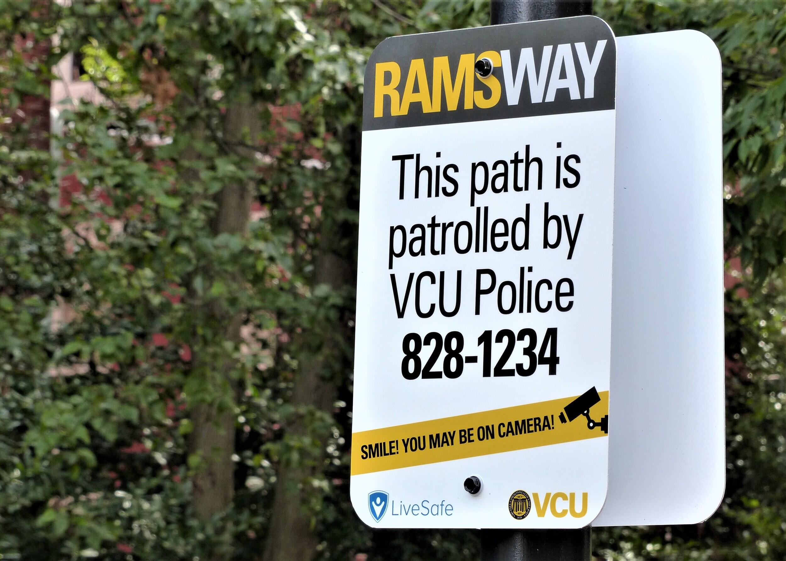 A sign stating "RAMSWAY. This path is patrolled by V C U Police. 828-1234. Smile! You may be on camera!" The V C U and LiveSafe logos are on the bottom of the sign.