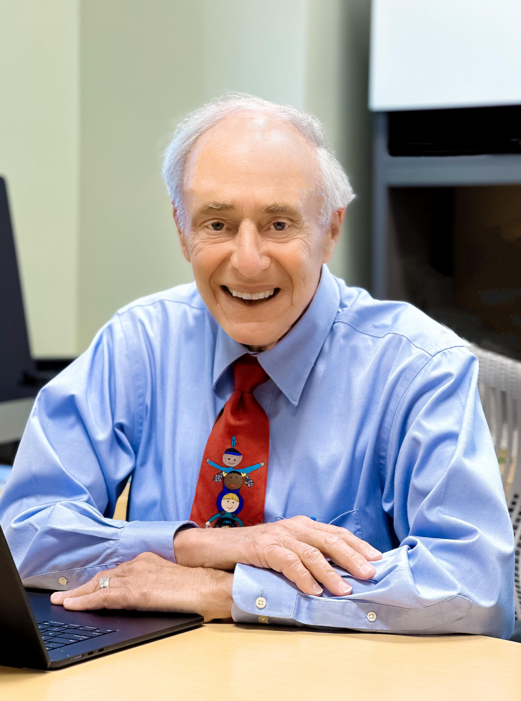 A photo of a man sitting at a desk with his arms crossing in front of him on the desk. 