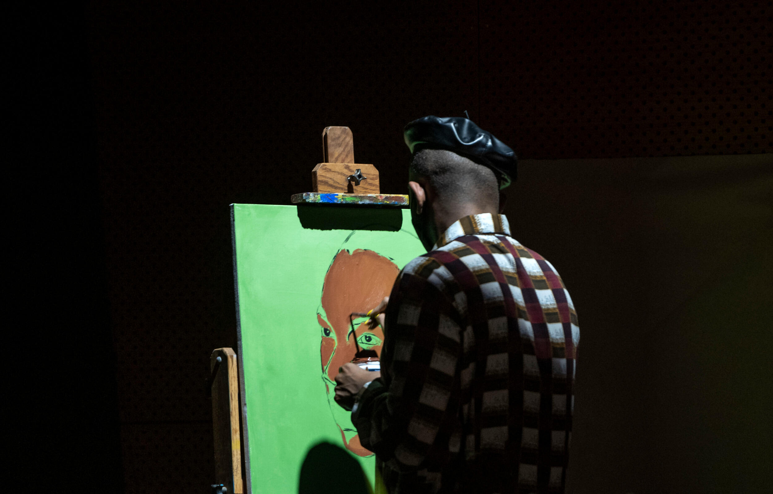 A painter with his back to the camera works on a painting with green background