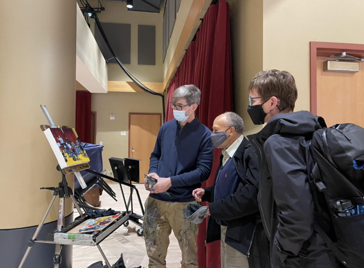(Left to right) Matt Lively and musicians Russell Wilson and Mary Boodell of the Richmond Symphony. They are all wearing face masks and looking at a painting on an easel. 
