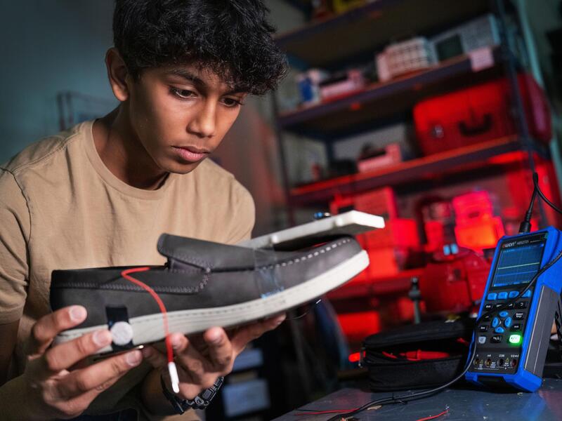 A photo of a teenage boy holding a shoe with a wire on it. 