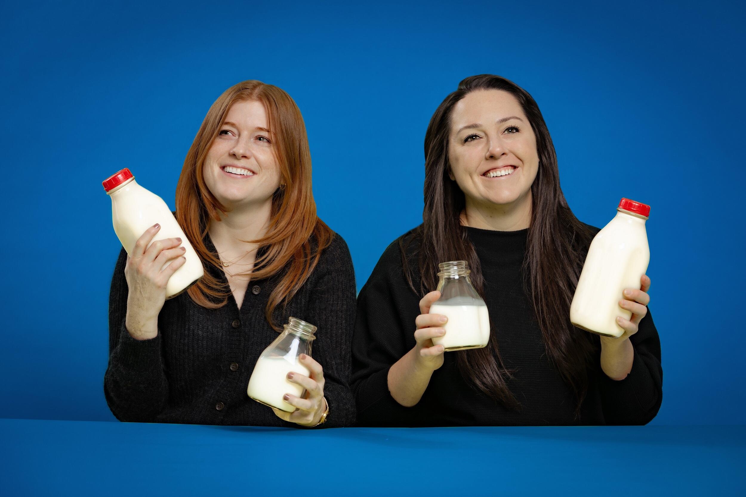 Two women wearing black shirts holding a container of milk in each hand