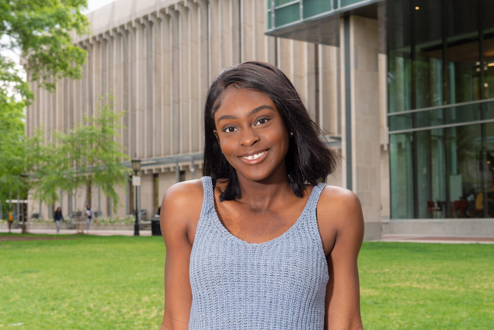 A smiling person in a gray tank top, in front of Cabell Library.