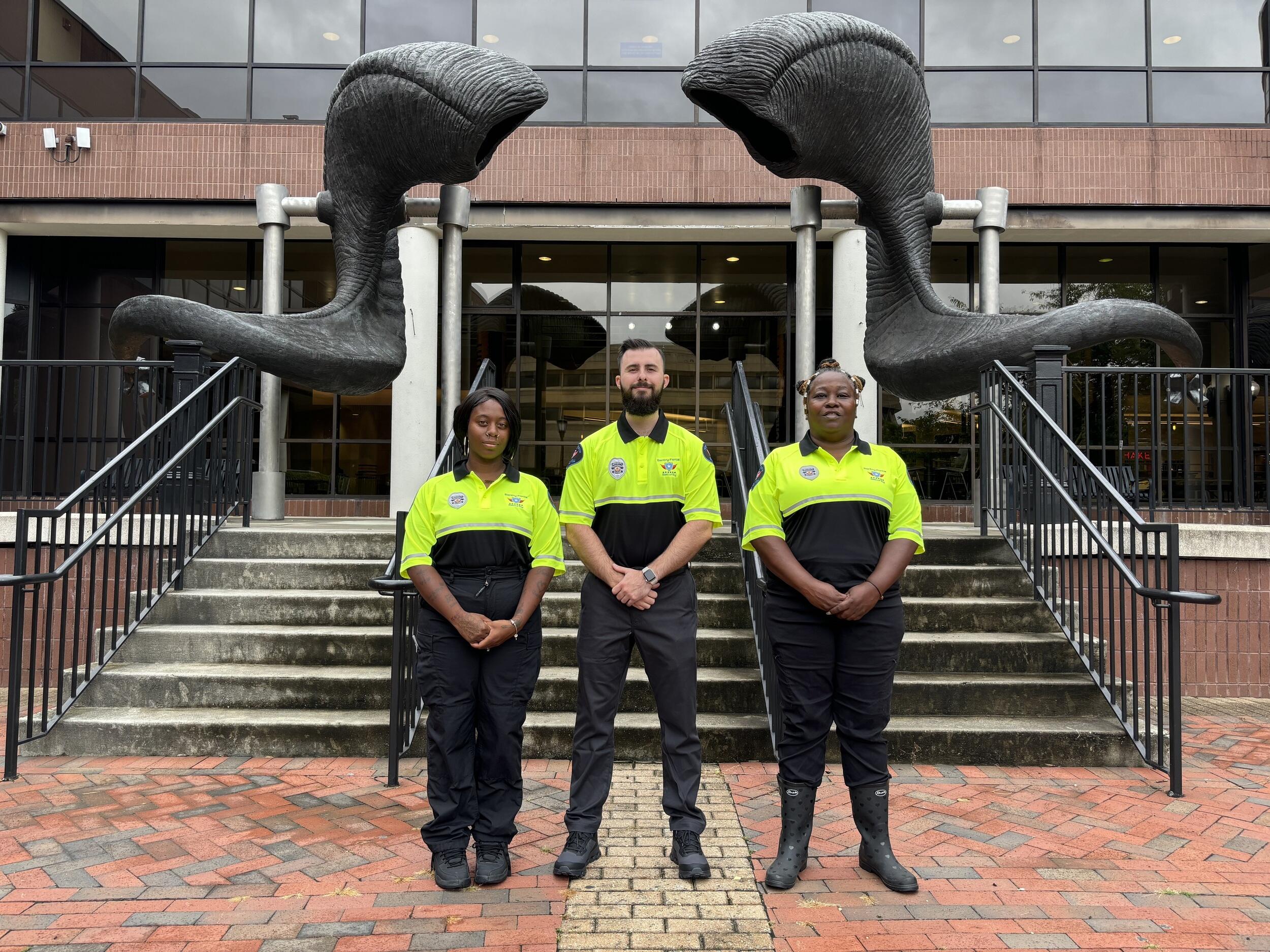 A photo of three officers standing outside in front of a staircase with a ram horns statue at the top of the staircase. 