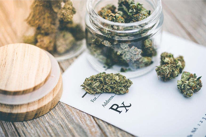 A photo of an open jar full of marijuana on top of a piece of paper for a prescription.